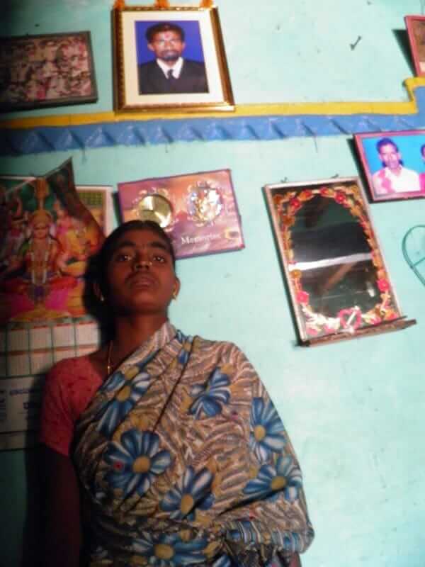 25-year-old Shanthamma, standing underneath a photo of her husband, Rama Krishna.