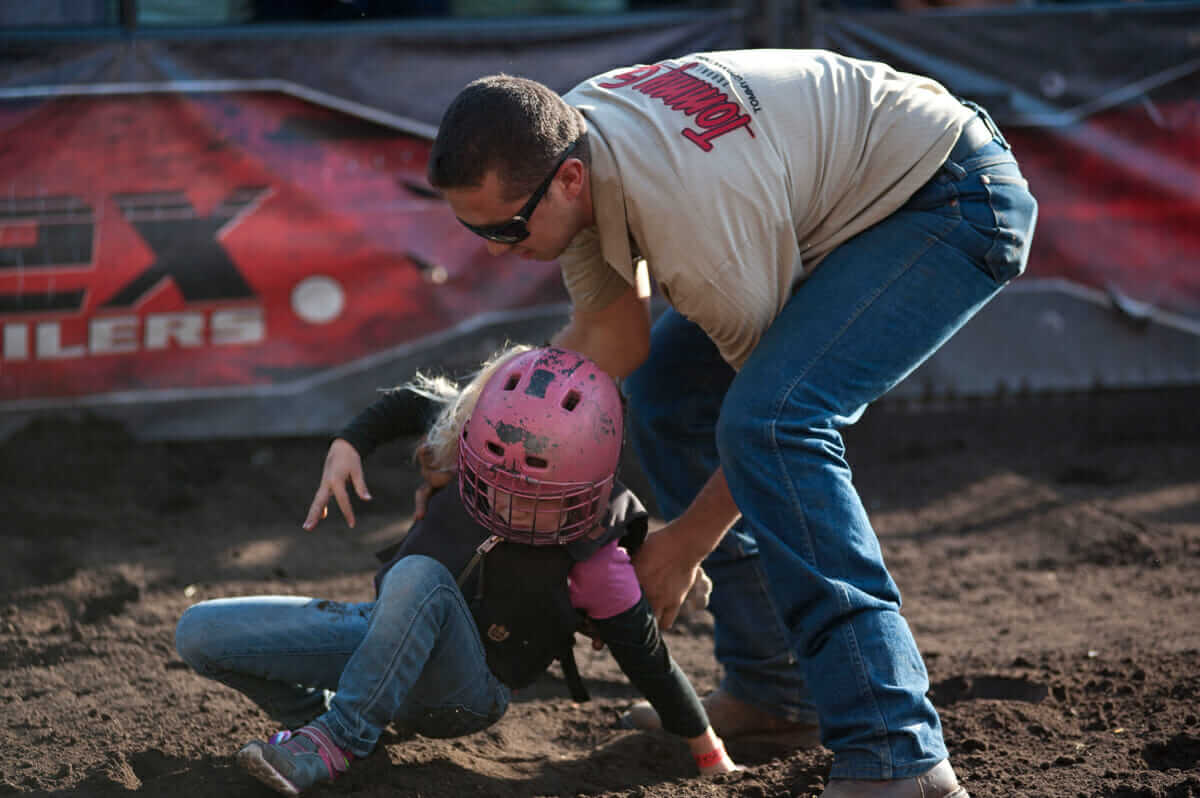 A Tommy G Productions employee helps a fallen rider up after her go at mutton busting.