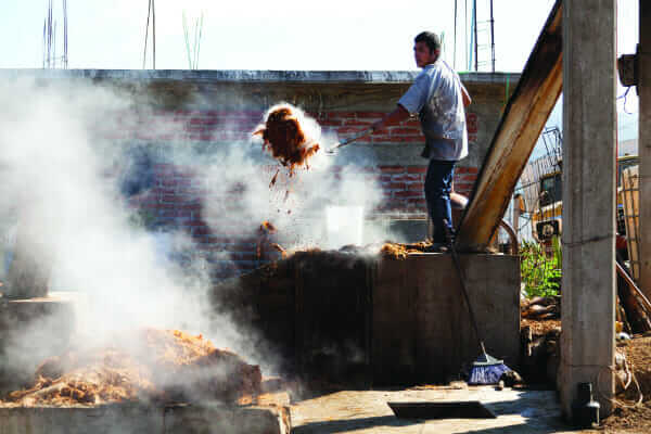 After the agave plants have been harvested, the remains are ground into a fibrous pulp called bagazo that will be heated and used in the mezcal-making process. A worker removes hot bagazo from a furnace.