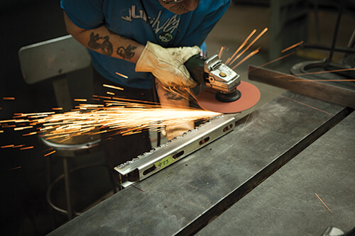 A welder grinds the back edge of a V-channel surface flush.