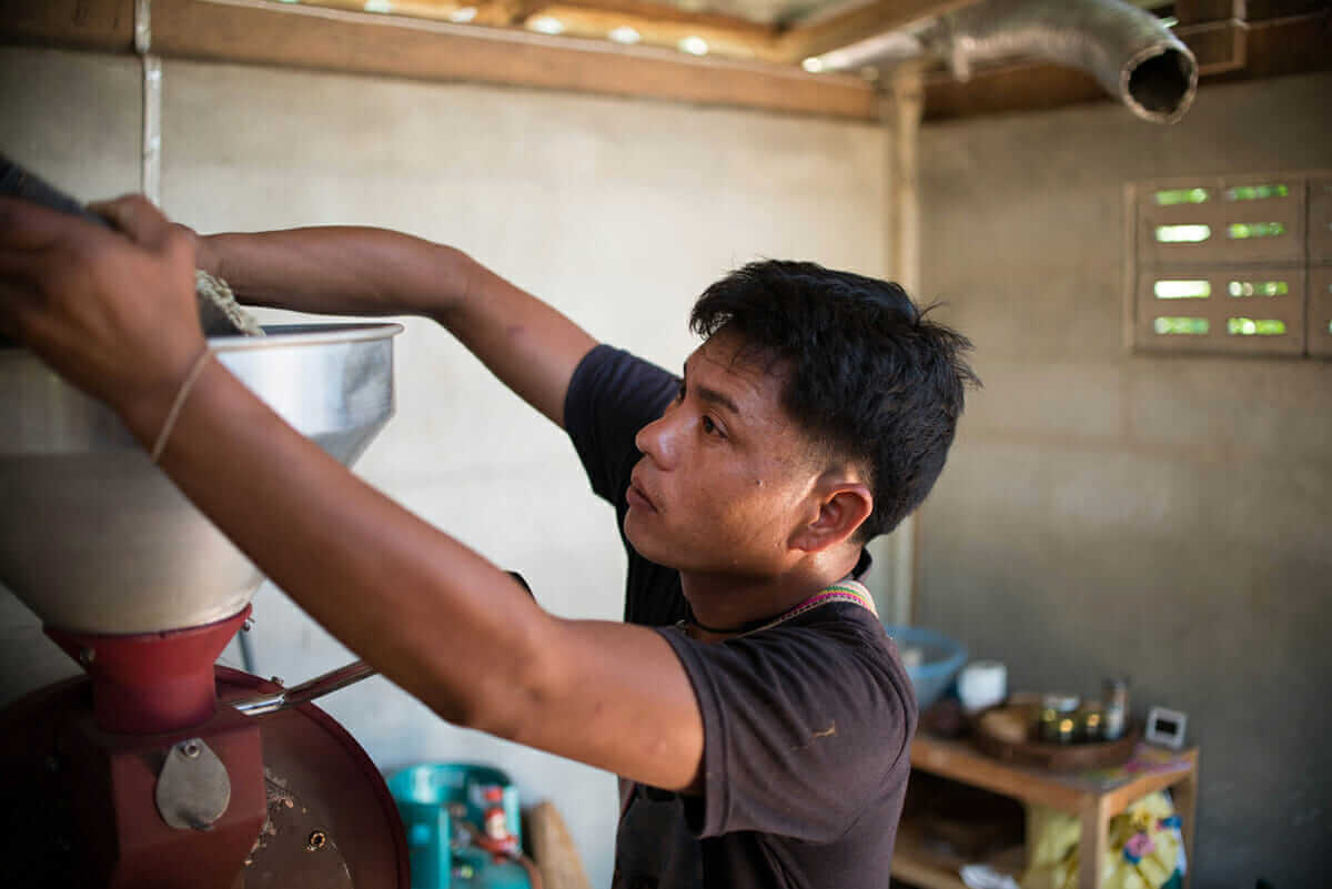 Lo-Ue Jayo, the head farm worker and Lahu tribesmen, feeds coffee beans into the coffee roaster.