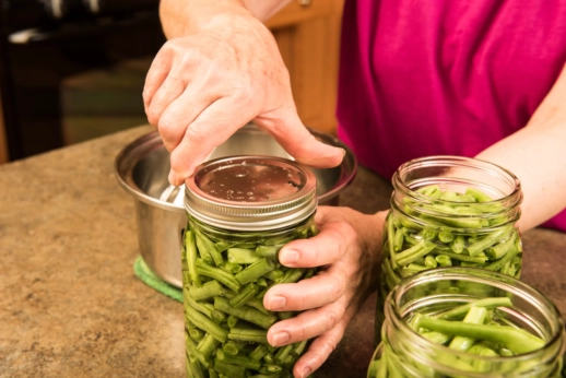 A person screws the cap onto a jar of green beans.