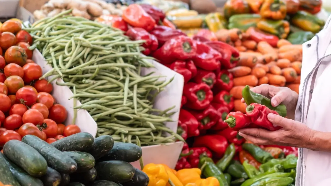 Close up of a produce stand with a variety of vegetables including peppers, asparagus, carrots, zucchini, and others neatly stacked in high piles.