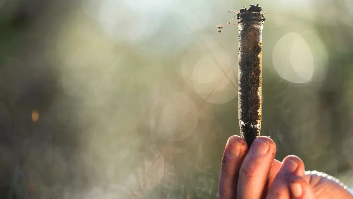 Close-up of a man's hand holding a small flask filled with dark soil for a post harvest test.