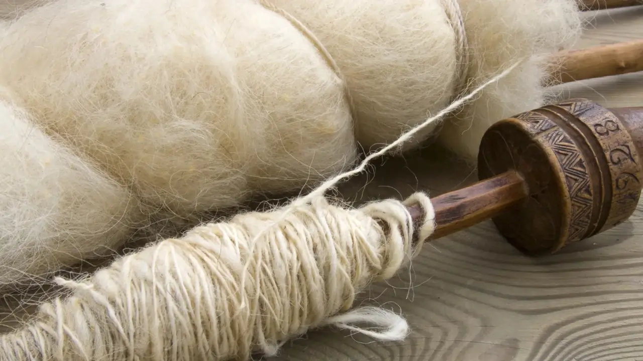 Soft, unspun wool lies in a loose roll beside freshly spun yarn neatly wound around smooth wooden spindles. 