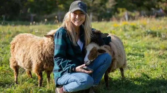 Melissa Schneider sitting down to pet animals and showcase sheep regeneration, appearing to be in a sunny area with green grass