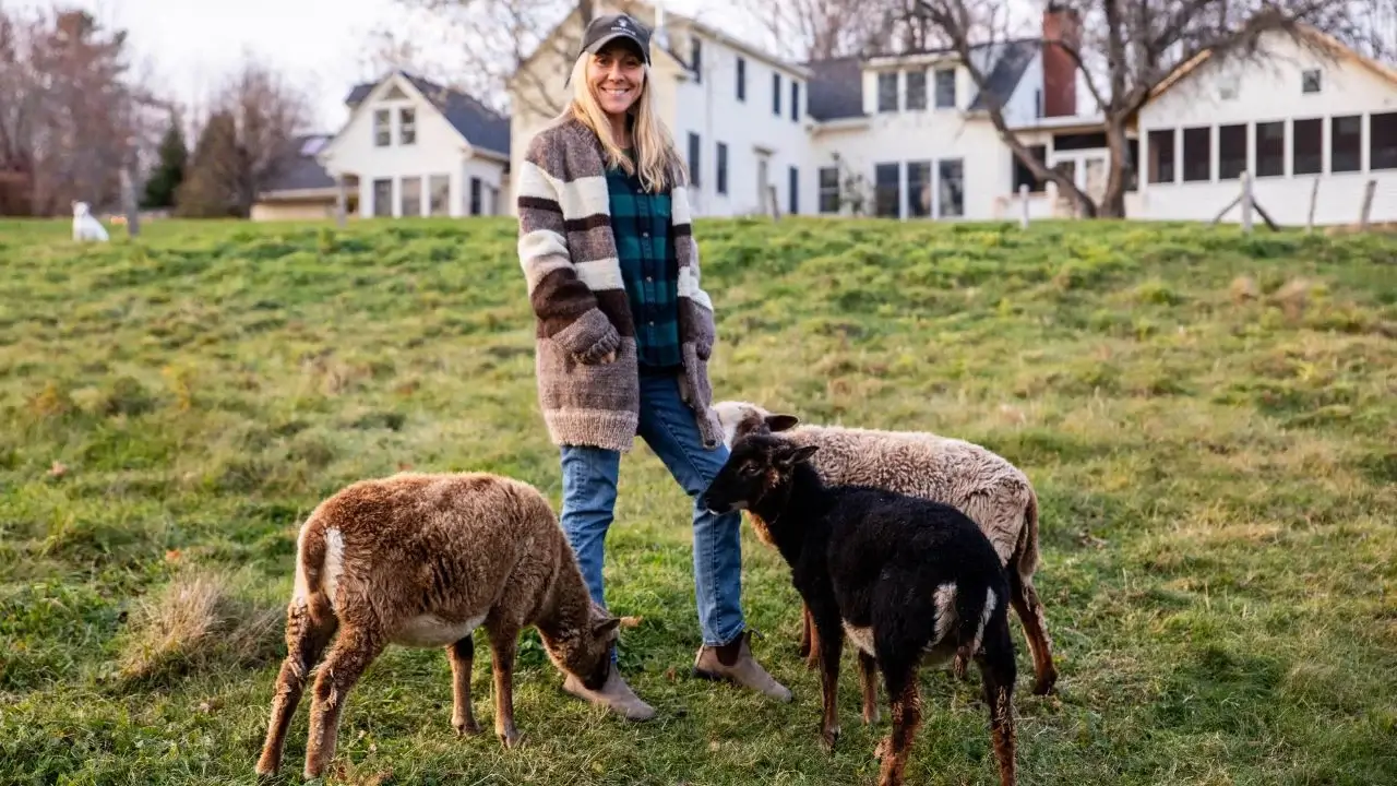 Melissa Schneider standing in an area with green grass, while three young animals stand surrounding her with houses visible in the background